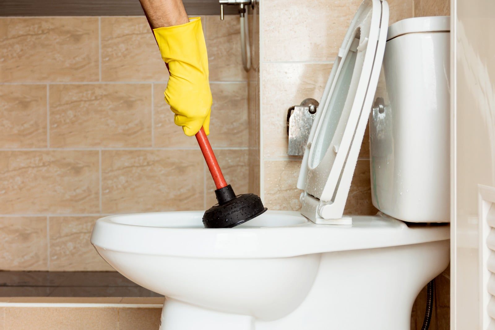 Hånd i gul handske holder en toiletsuger nede i toilettet